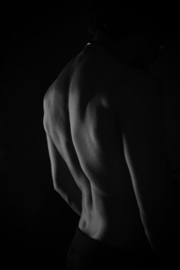pexels-photo-19724586-19724586 Black and white artistic portrait focusing on the muscular back of a topless man in shadow.