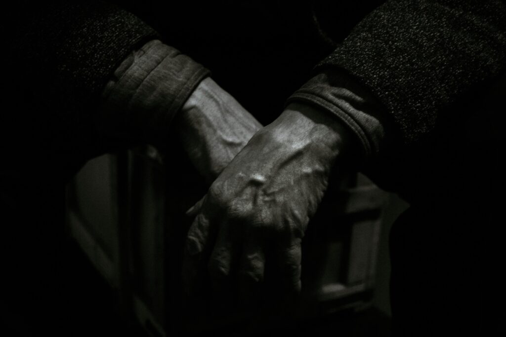 Dramatic black and white close-up photo showcasing aged hands folded together, expressing emotion and texture.